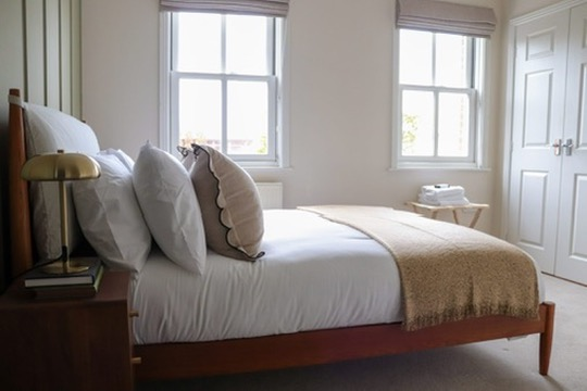 Finished guest bedroom with wooden bed frame and layered linens after refurbishment