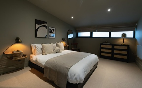 Finished loft double bedroom with dark walls and rattan drawers after renovation