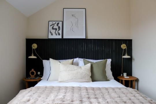 Boutique attic bedroom with black panelled headboard and brass wall lights after renovation