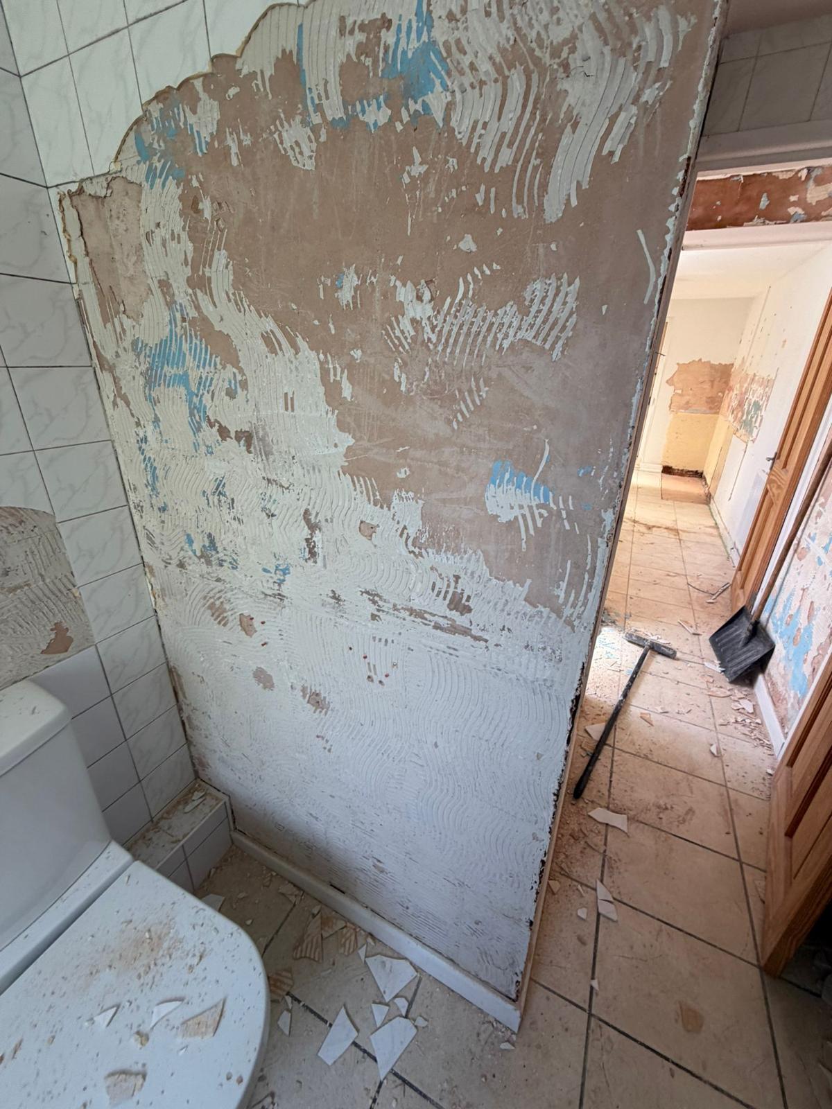 Bathroom wall with exposed plaster and debris before works