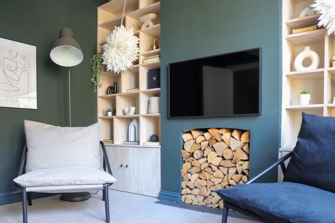 Finished green living room with bespoke joinery and log-store fireplace after renovation
