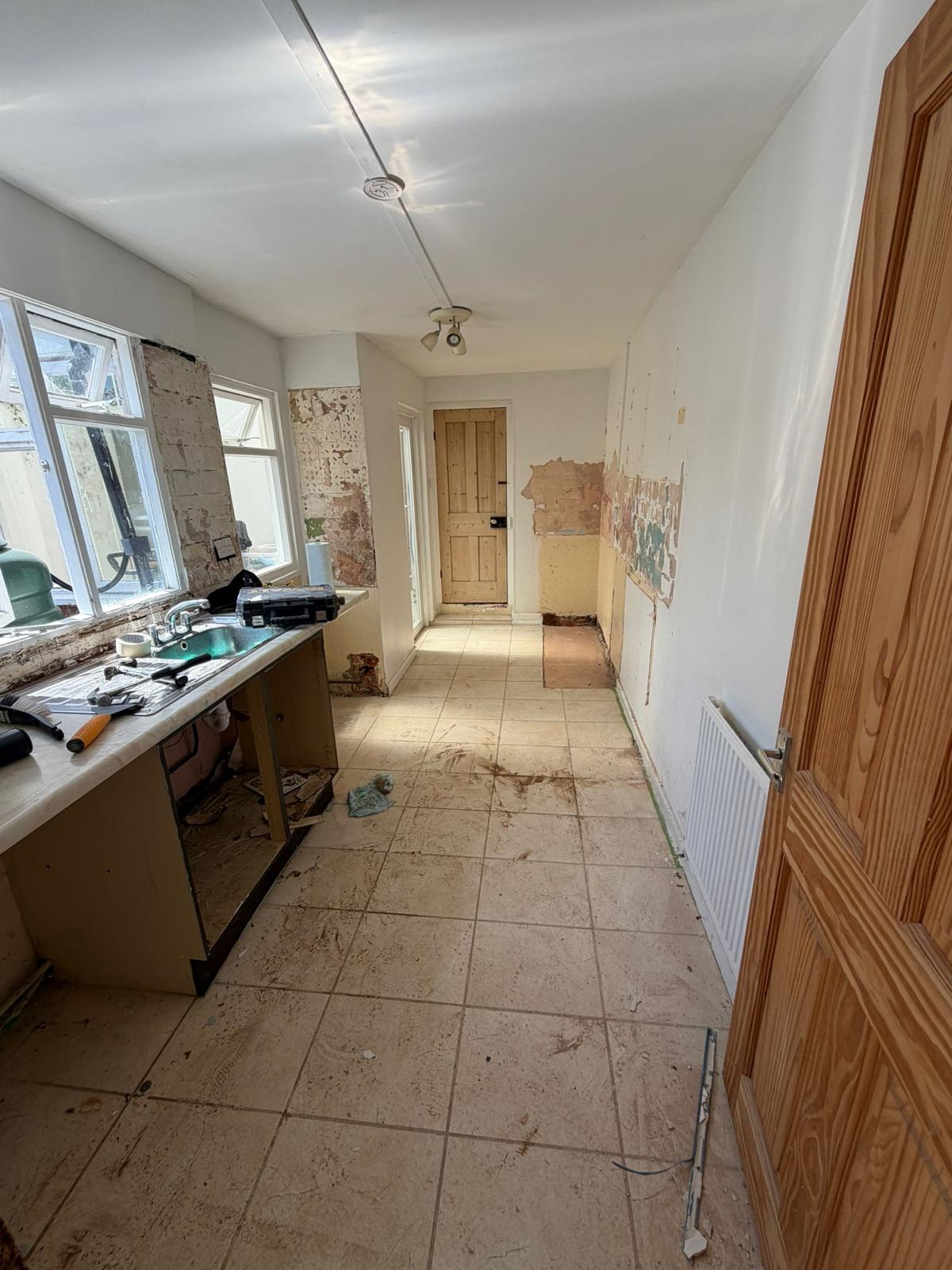 Stripped galley kitchen with exposed plaster before refurbishment